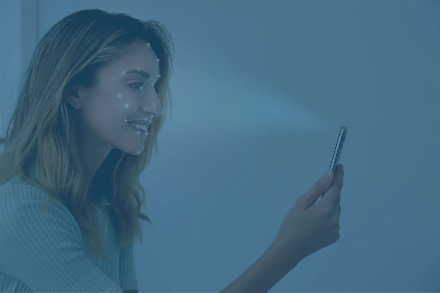 A woman is holding a smartphone in her hand, smiling as she uses facial recognition technology. Her face is overlaid with a digital grid pattern, indicating the scanning process, against a blue-tinted background. . In a demo creation process.